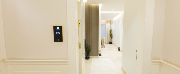 Een gang met een bord dat kamer F3 aangeeft, een potplant en een deur aan het einde.