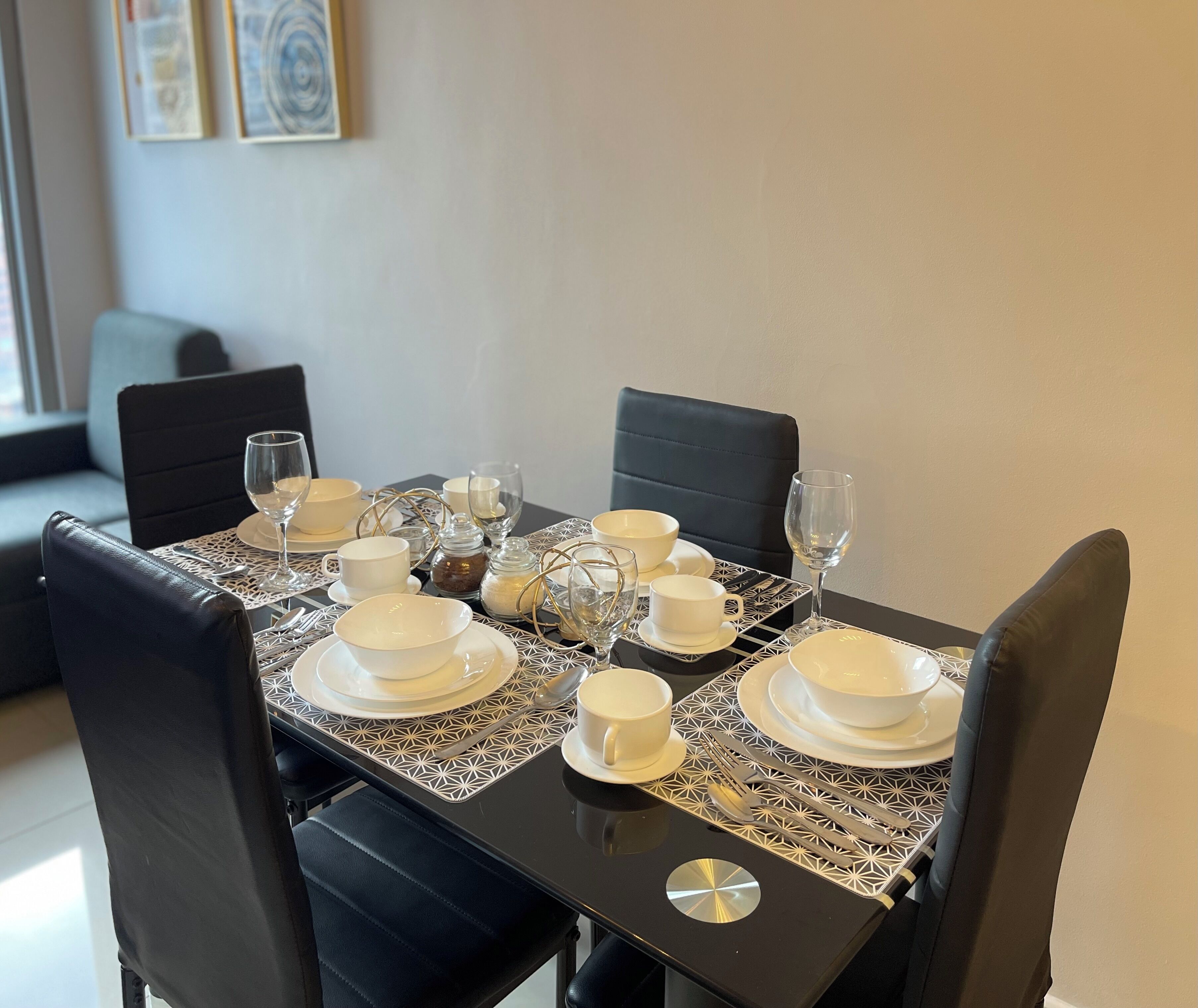 A dining table set with white plates, bowls, and glasses, surrounded by black chairs.