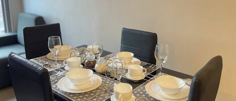 A dining table set with white plates, bowls, and glasses, surrounded by black chairs.