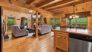 A log cabin interior with a wooden floor, a kitchen with a dishwasher, a dining area with a table and chairs, and a living room with a sofa and a fireplace. - Triple Mountain View Stunning 4 BDR Cabin w/ Private Hot Tub, Game Room (Gatlinburg)