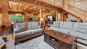 A log cabin interior with a dining area, two sofas, a coffee table, and a kitchen. - Triple Mountain View Stunning 4 BDR Cabin w/ Private Hot Tub, Game Room (Gatlinburg)