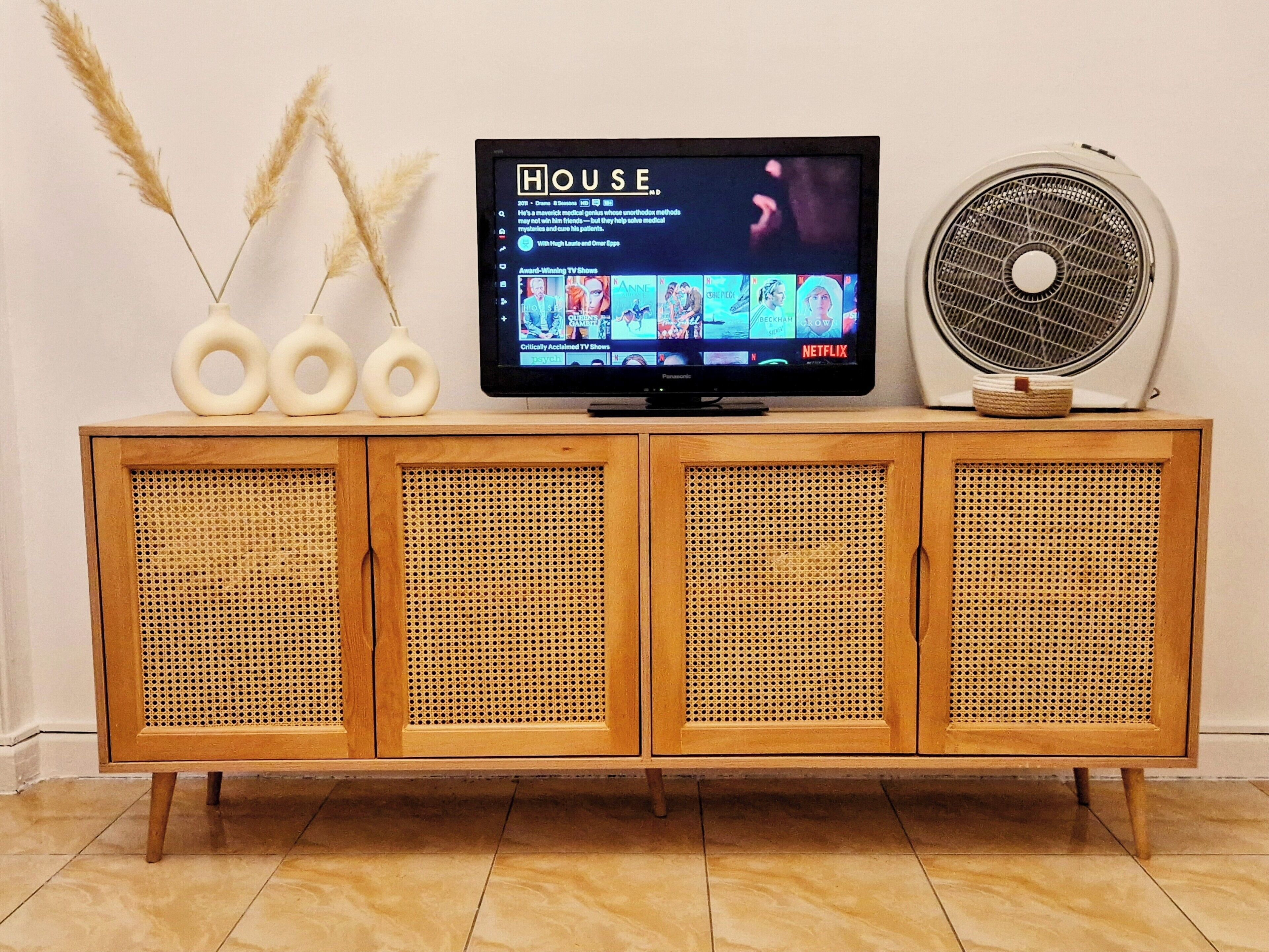 A wooden entertainment center with a television displaying a streaming service interface, a fan, and decorative items.