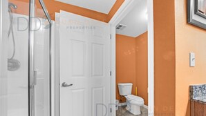 Un baño con puerta blanca, ducha y pared naranja.