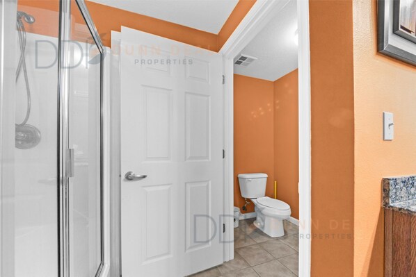 A bathroom with a white door, a shower, and an orange wall.