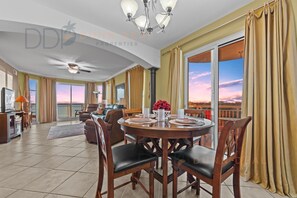 A spacious living room with a dining area, large windows, and a balcony with a view. - Legacy Tower II 609 | Stunning Coastal Views! (Gulfport)