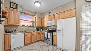 A kitchen with wooden cabinets, a white refrigerator, a microwave, a stove, and a dishwasher. - Legacy Tower II 609 | Stunning Coastal Views! (Gulfport)