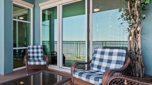 A balcony with wicker chairs, a glass table, and a view of the sea. - Legacy Tower II 907 | Deluxe Unit with Stunning Coastal Views! (Gulfport)