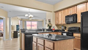 A modern kitchen with wooden cabinets, a black refrigerator, and a microwave. - Legacy Tower II 907 | Deluxe Unit with Stunning Coastal Views! (Gulfport)