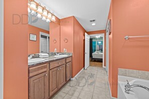 Une salle de bain avec deux lavabos, des meubles en bois, un meuble-lavabo, une baignoire et un espace douche.