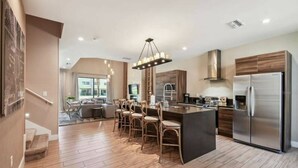 A modern kitchen with a central island, stainless steel appliances, and a dining area with wooden chairs. - DLuxx Magic Jacuzzi Home 3 miles from Disney 7454 (Kissimmee)