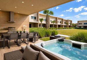 Un patio exterior con jacuzzi, zona de comedor y vista a un edificio de varios pisos.