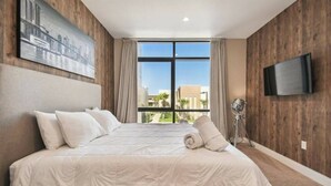 A hotel room with a large bed, a flat-screen TV, and a view of buildings through the window. - DLuxx Magic Jacuzzi Home 3 miles from Disney 7454 (Kissimmee)