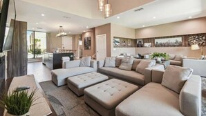 A spacious living room with a large sectional sofa, a flat-screen TV, and a dining area with a kitchen in the background. - DLuxx Magic Jacuzzi Home 3 miles from Disney 7454 (Kissimmee)