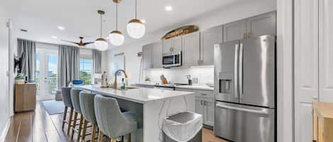 A modern kitchen with stainless steel appliances, a central island with bar stools, and a view of the outdoors.