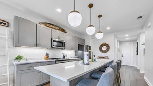 A modern kitchen with grey cabinets, a central island with bar stools, pendant lighting, and a microwave. - ☀️Short Walk to Beach-Pools-30A-Gulf Place Residences 203 (Santa Rosa Beach)