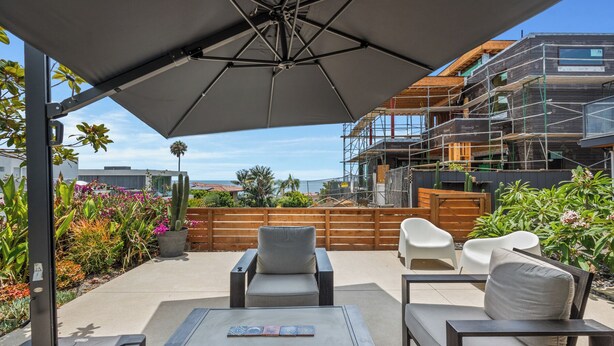 A patio with outdoor furniture, a large umbrella, and a view of a building under construction. - Partial Ocean Views/Walk to All/Great Location! (La Jolla)