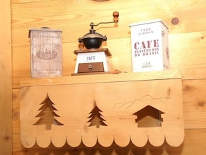 A wooden shelf with a coffee grinder, a box labeled "CAFE PLANTATIONS DE BRASIL," and a wooden box with tree and house cutouts. - Log cabin near Gerardmer (Rochesson)