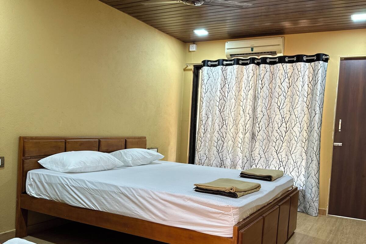 A bedroom with a wooden bed, a bedside table, a wardrobe, a ceiling fan, and a window with a curtain.