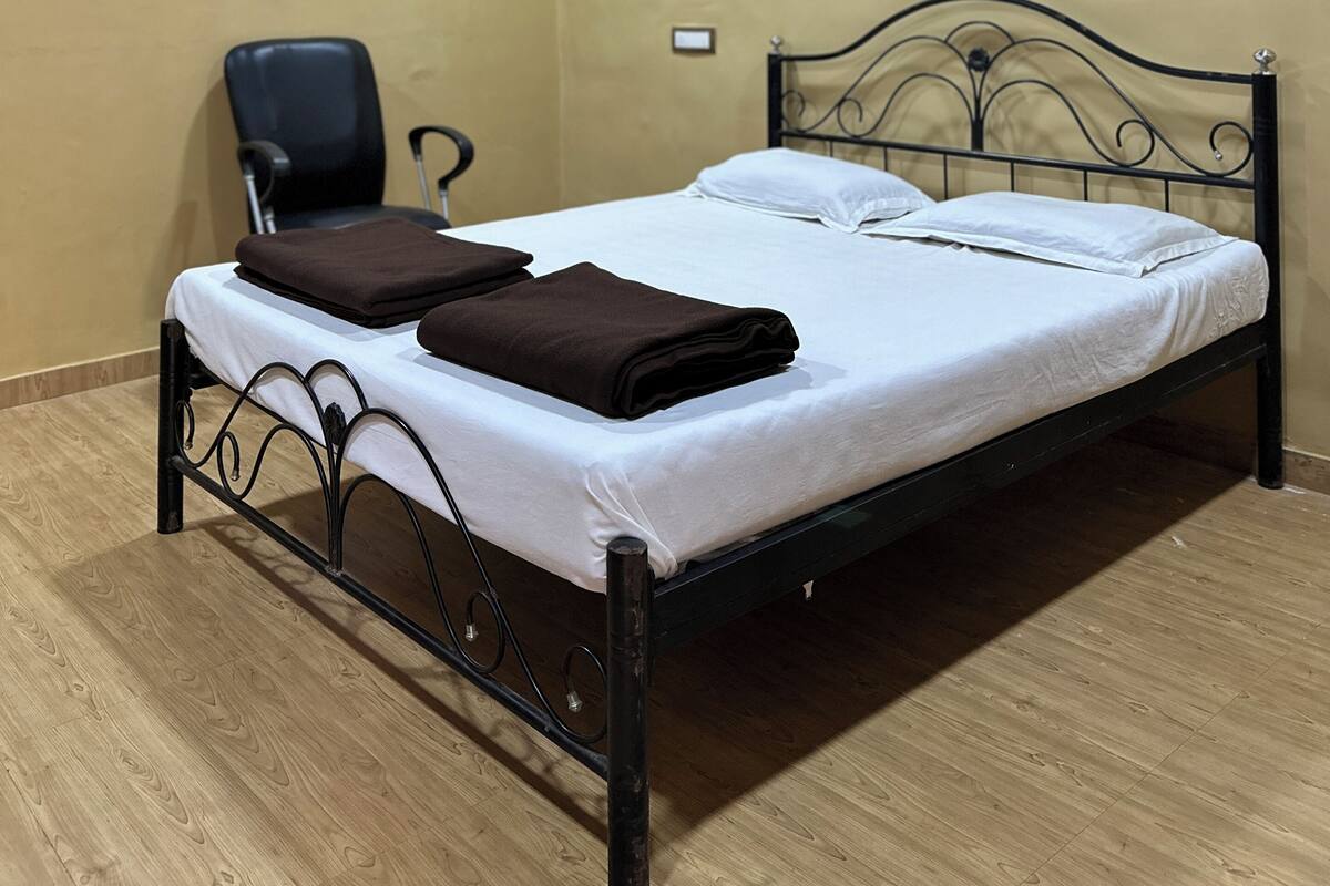 A single bed with a metal frame, a ceiling fan, and an air conditioning unit on the wall.