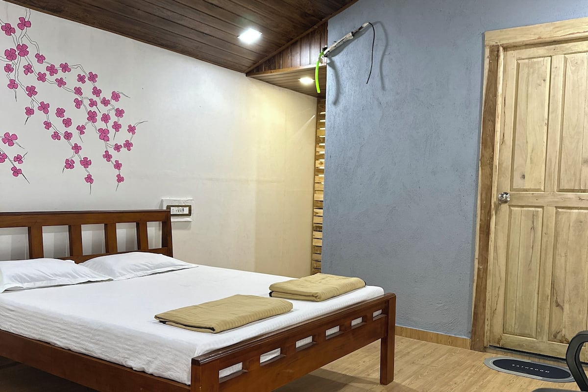 A bedroom with a wooden bed, a ceiling fan, a wall-mounted light, and a wooden door.