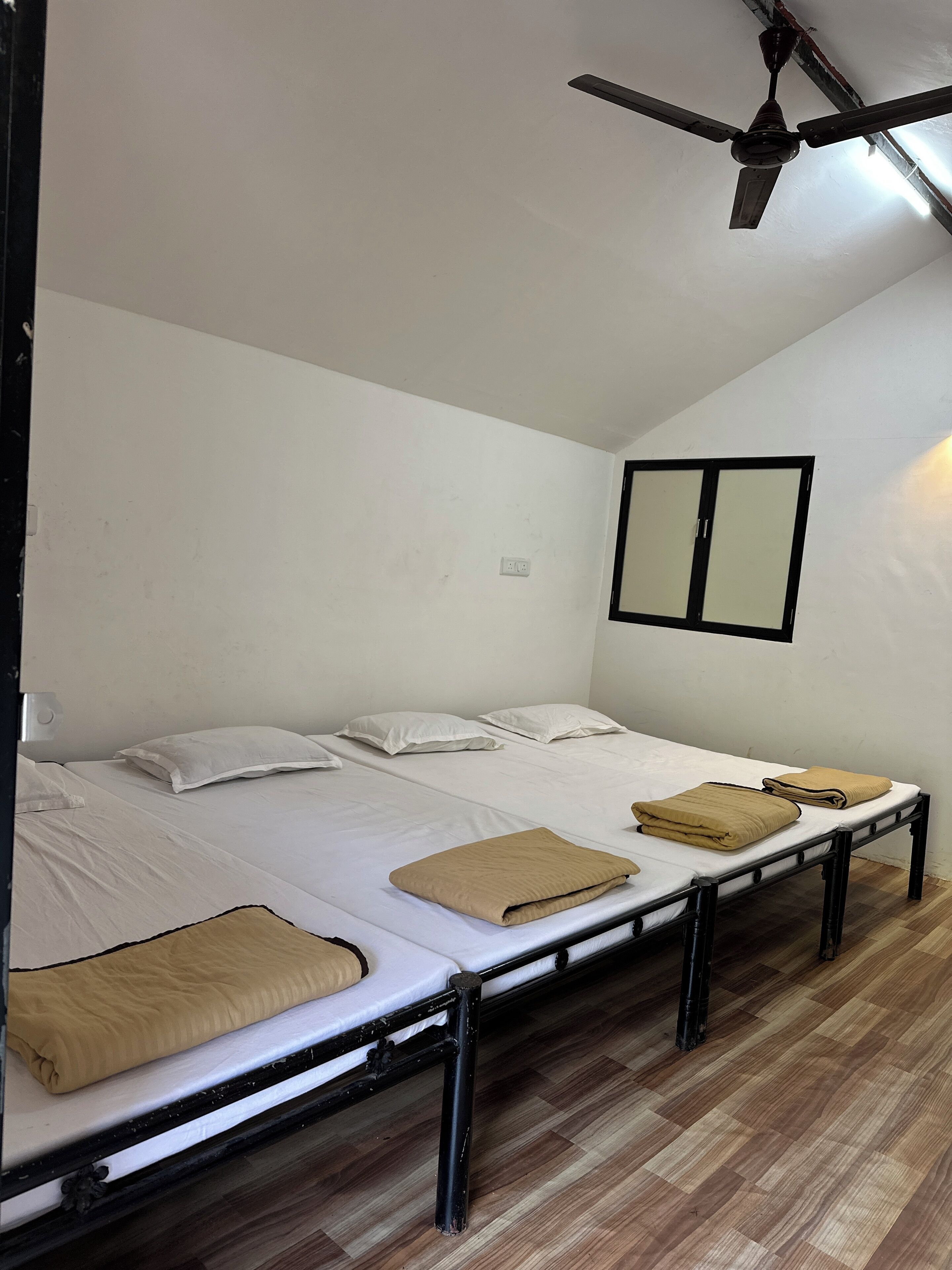 A room with two single beds, a ceiling fan, and a window with blinds.