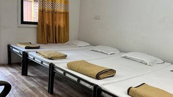 A dormitory room with two single beds, a window with patterned curtains, and a wooden floor.