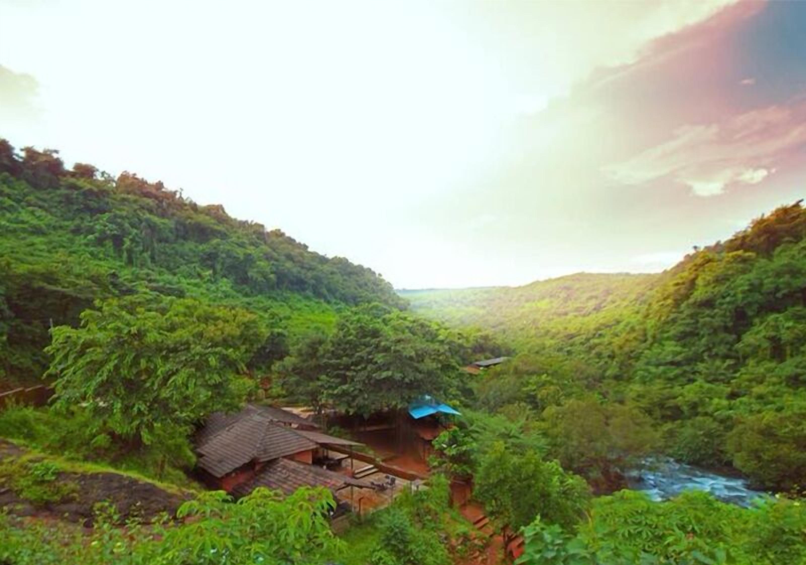 A lush green valley with a small house and a river.