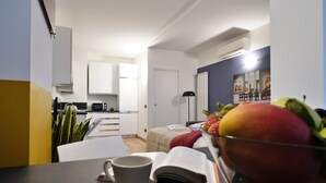 Un espacio habitable compacto con kitchenette, una zona de comedor con una mesa y una taza, y una cama con un cojín rojo.
