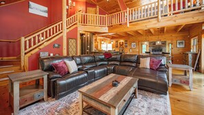Un vaste salon doté d’un grand canapé en cuir en forme de L, d’une table basse en bois et d’un escalier en bois menant à un niveau supérieur.