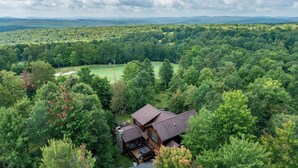 Une grande cabane rustique, entourée d’une forêt dense, avec vue sur des montagnes lointaines et un terrain de golf.