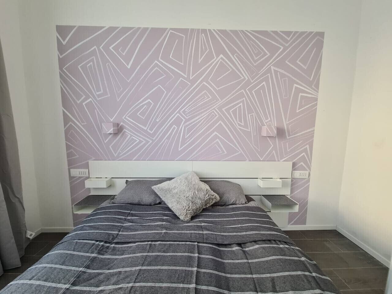 Ein Schlafzimmer mit einem Bett, einem Kopfteil mit Einbauregalen und einer Wand mit Muster.
