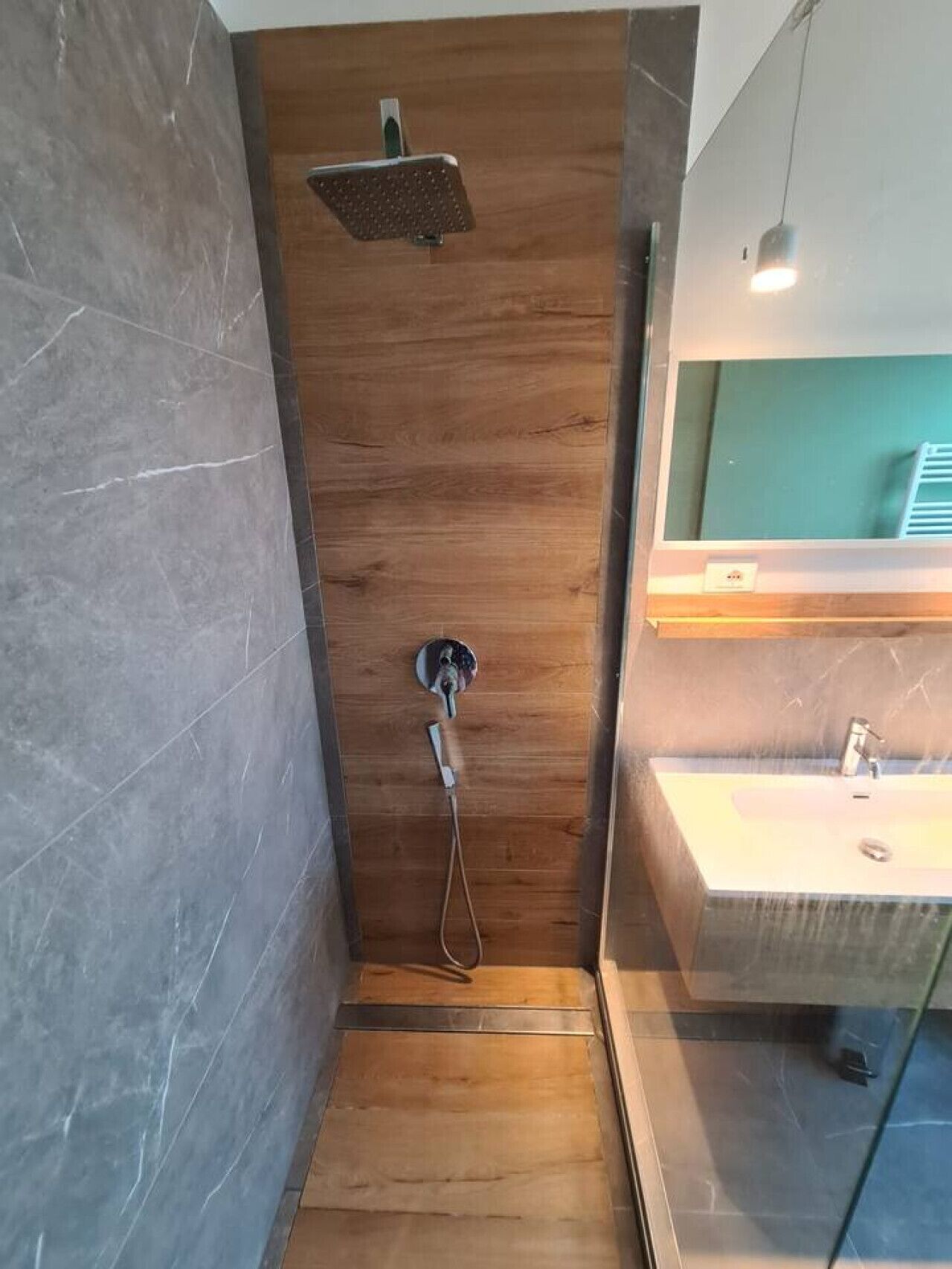 Un bagno moderno con cabina doccia in legno, soffione a mano e lavabo con specchio.