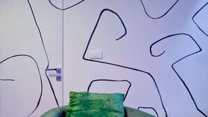 Ein grüner Sessel mit grüner Sitzkissen in einem Raum mit weißer Wand und abstrakten, schwarzen Linienzeichnungen.
