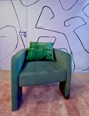 Un sillón verde con un cojín verde en una habitación con pared blanca y dibujos lineales negros abstractos.