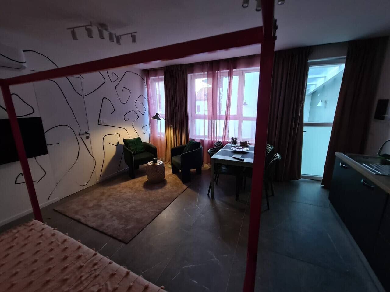 Ein Zimmer mit Etagenbett, Esstisch, Küchenzeile und Blick durch große Fenster nach draußen.