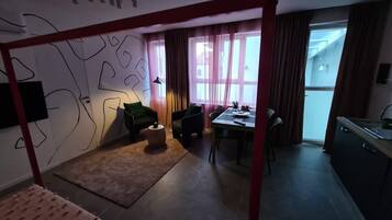 Ein Zimmer mit Etagenbett, Esstisch, Küchenzeile und Blick durch große Fenster nach draußen.