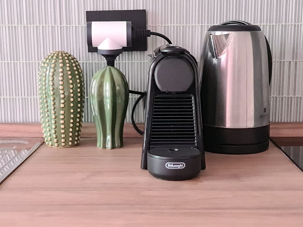 A kitchen counter with a coffee maker, a kettle, and a cactus.