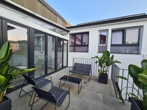 Une terrasse sur le toit dotée d’une balustrade en verre, de deux chaises longues, d’une petite table et de plantes en pot.