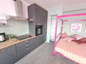Une chambre compacte comprenant un lit, une kitchenette et une salle de bain.