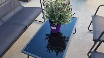 A balcony with a blue glass table, two black metal chairs, and a purple potted plant with purple flowers.