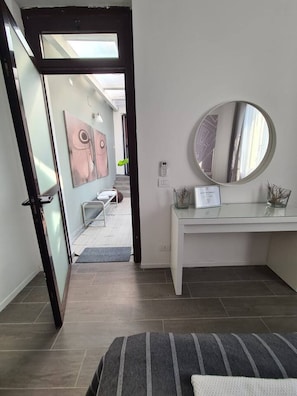 Une chambre à coucher moderne avec un lit, un miroir rond, une commode blanche et une porte en verre donnant sur une salle de bain.