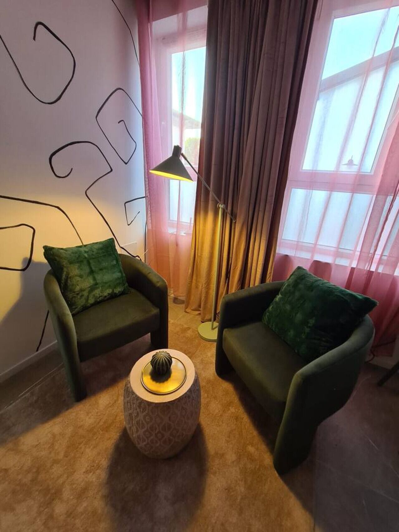 Ett rum med två mörkgröna fåtöljer, ett runt sidobord med ett dekorativt föremål och en golvlampa.