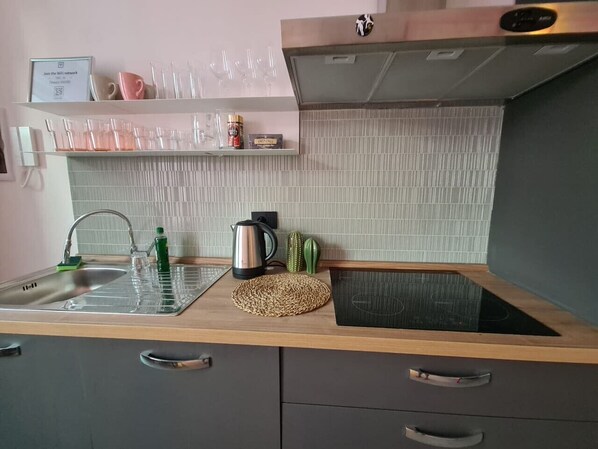 Une cuisine équipée d’un évier, d’une bouilloire, d’un tapis et d’une étagère avec des verres et un panneau.