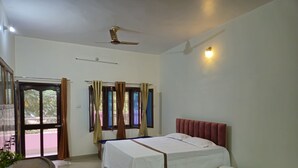 Une chambre à coucher avec un lit, un ventilateur de plafond, une fenêtre avec des rideaux et une petite table sur laquelle est posée une plante.