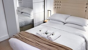 A neatly made bed with white linens and a brown throw blanket, a bedside table with a lamp, and a wardrobe with a mirror.