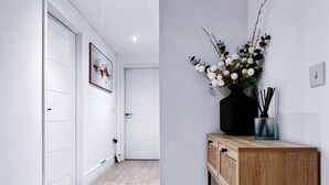 A modern hallway with a wooden floor, white walls, and a wooden console table with a vase of flowers.