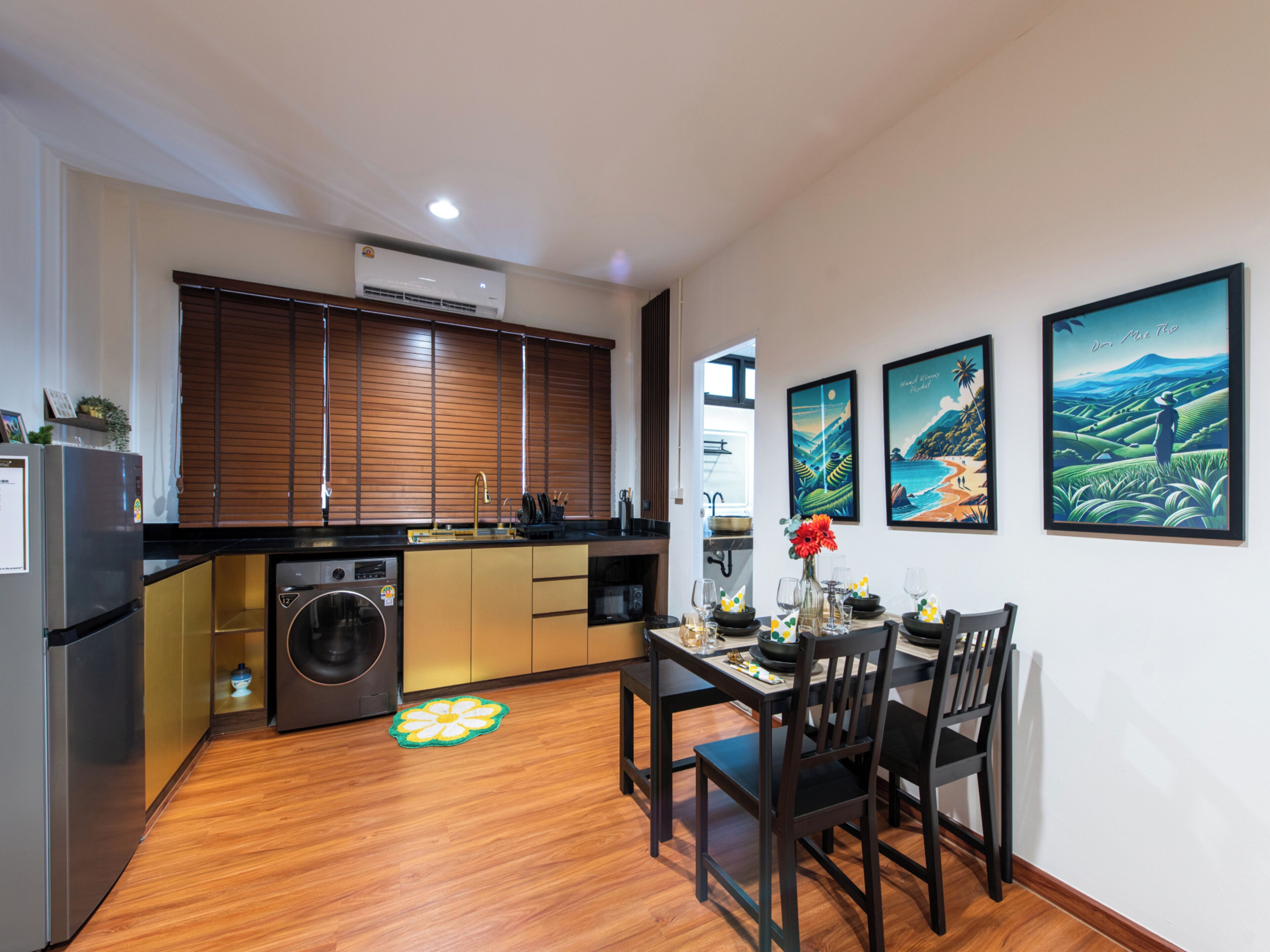 A compact kitchen with a built-in washer, a dining area with a table and chairs, and three framed artworks on the wall.