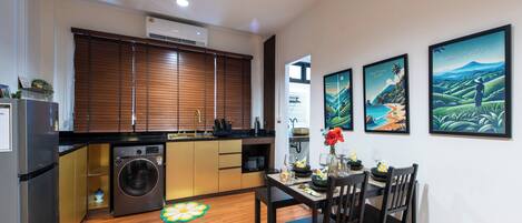 A compact kitchen with a built-in washer, a dining area with a table and chairs, and three framed artworks on the wall.