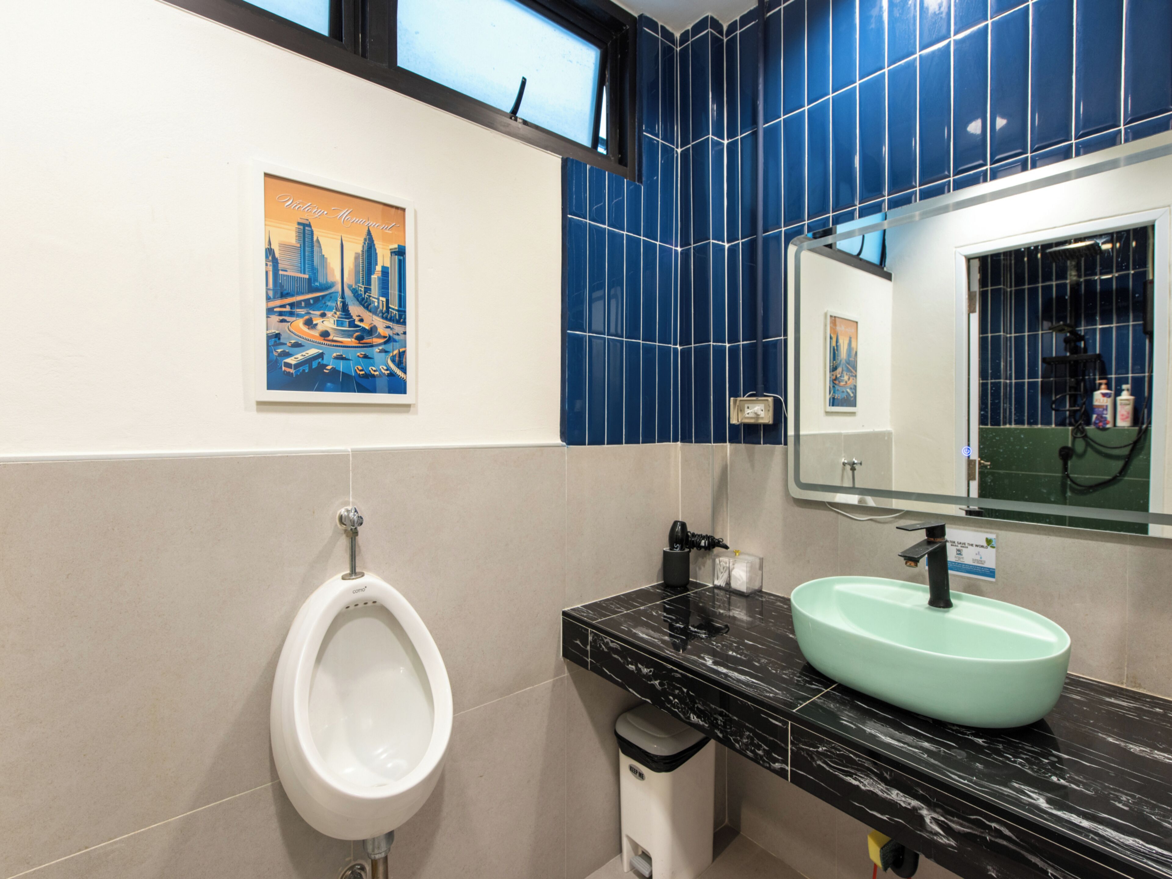 Une salle de bain moderne avec un urinoir, un lavabo doté d’un bac vert, un miroir et un mur recouvert de carreaux bleus.