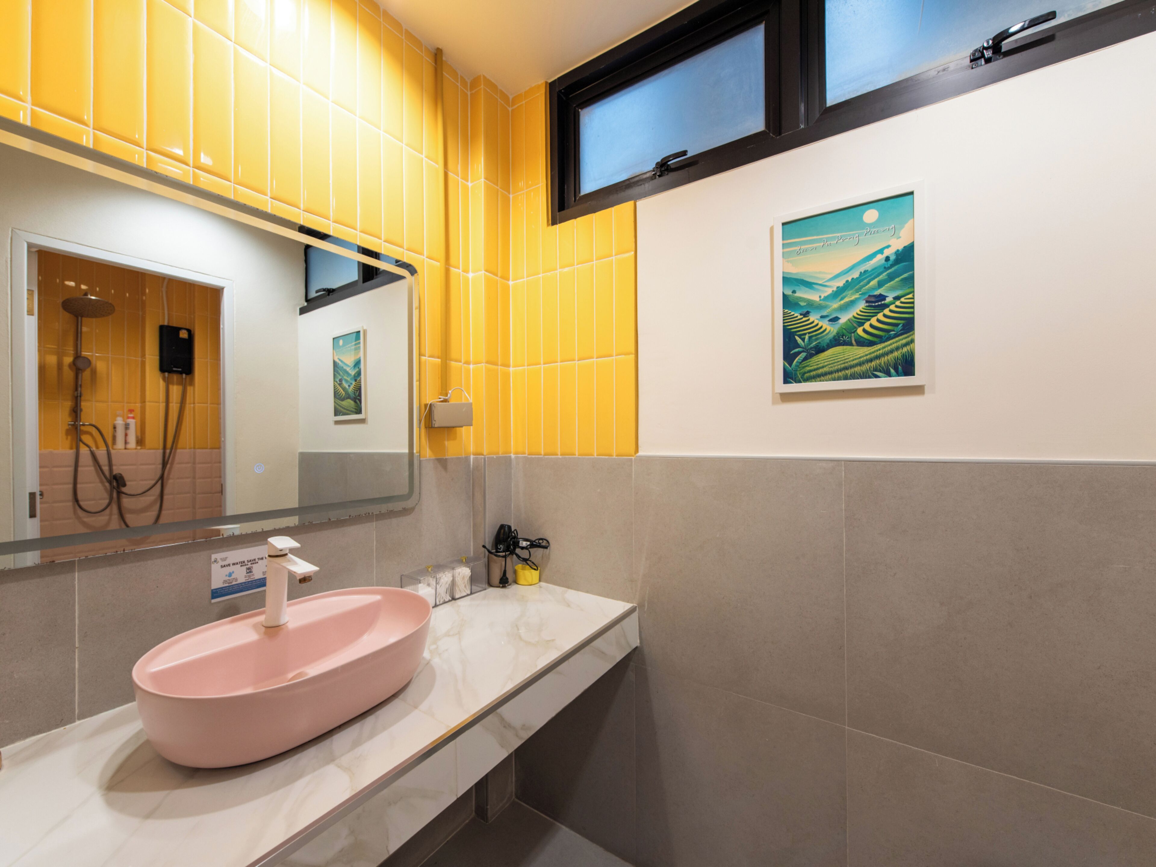 Un baño con un lavamanos rosa, azulejos amarillos, una ventana y un cuadro en la pared.